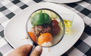Image shows a plate of food components under a magnifying glass on top of a black and white checkered cloth Image shows a plate of food components under a magnifying glass on top of a black and white checkered cloth