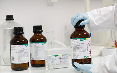 Karl Fischer Titration Series Cover picture representing a webinar on 'Karl Fischer Titration Series' showcasing three brown colored reagent bottles, with one transparent bigger bottle at their back and gloved hands of a lab chemist wearing a lab coat opening ampoules with two ampoules kept outside their box.