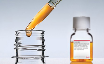 FBS Serum Serum bottle in the background halfway filled with golden liquid. In the foreground, a pipette partially filled with gold liquid is pulling out of a bottle top and dripping.