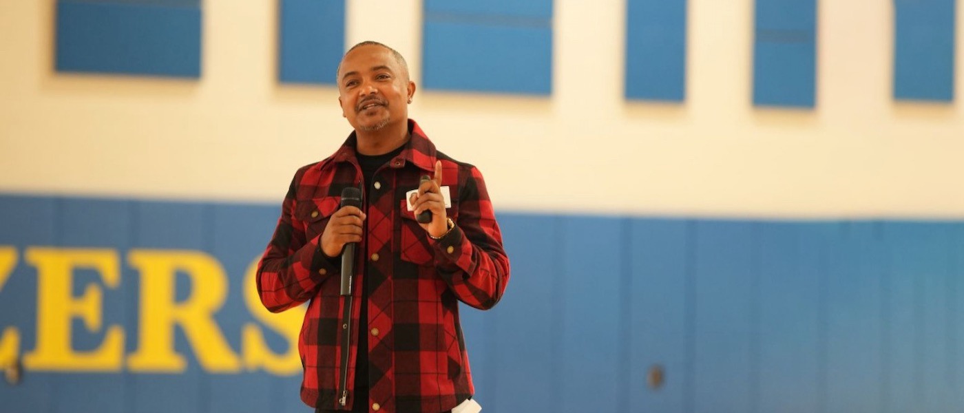 Abdi Wege wears a red flannel and holds a microphone in his right hand. Abdi Wege wears a red flannel and holds a microphone in his right hand.