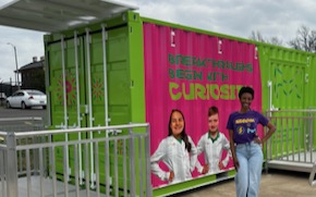 Danielle Chavis Curiosity Cube Danielle Chavis wears a SPARK t-shirt and stands in front of the Curiosity Cube which is bright green, has images of two young scientists with the words “Breakthroughs Begin with Curiosity” on the front.