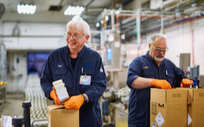 packaging line Two employees wear uniforms, gloves and safety glasses and package boxes.