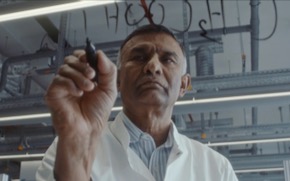 ponnusamy-green-chemistry Dr. Ponnusamy wears a lab coat is writes out chemical compounds on glass with a marker.