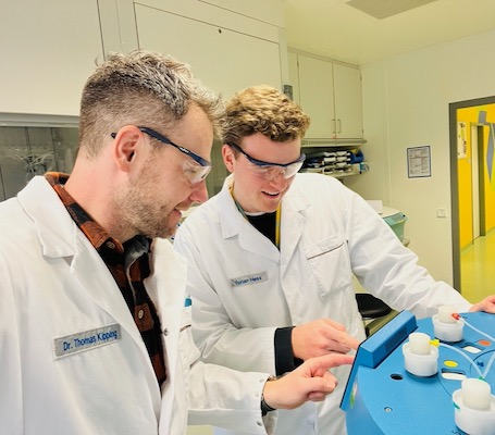Thomas Kipping and Florian Hess Thomas Kipping and Florian Hess work together on an instrument. They both wear safety glasses and look at the control panel .
