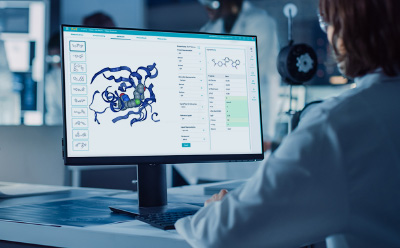Benefits for Medicinal Chemists 一位身着白大褂的科学家坐在办公桌前,与显示分子结构的电脑屏幕互动。屏幕上显示的是蛋白质或复合物的三维图像,边上有各种工具和数据选项。