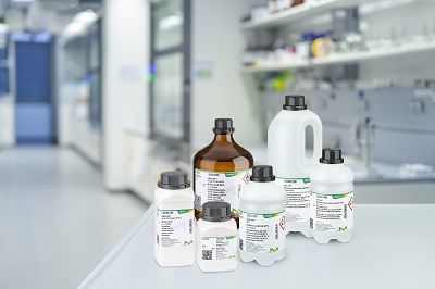 Emsure bottles A variety of laboratory Emsure solvent bottles, labeled with product information, placed on a white counter in a modern laboratory setting. The bottles vary in size and shape, with both amber and white bottles visible, representing different chemical solvents typically used in analytical and research labs. The background features lab equipment and shelves
