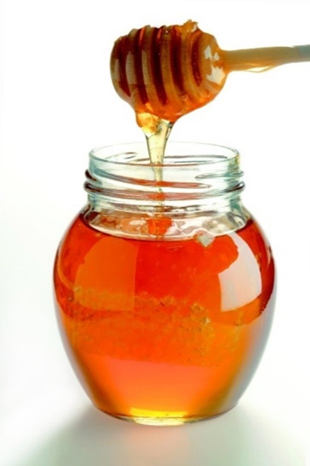 Glass jar filled with golden honey and honeycomb, with honey drizzling from a wooden dipper. Glass jar filled with golden honey and honeycomb, with honey drizzling from a wooden dipper.