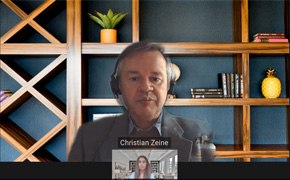 Christian Zane与另一位参与者的虚拟会议截图。小窗口显示另一位参与者正在发言。背景是秩序井然的架子，摆放着书籍、装饰品和盆栽。