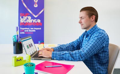 Photograph of scientist sitting at a desk in an office using Millicell® Cloud features to analyze data