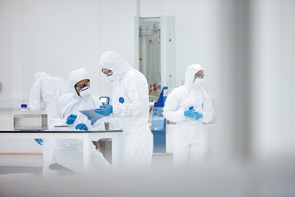 Two scientists wearing cleanroom attire discuss microbiology quality control (QC) test data 