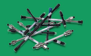 一系列Supelco<sup>®</sup> HPLC和 UHPLC 柱散落在绿色表面上。这些色谱柱为圆柱形，带有金属饰面，两端配备接头，代表着满足不同分析需求的一系列色谱柱技术。它们尺寸各异，一些有标记了规格或型号。