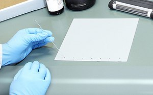 A person performing Thin Layer Chromatography (TLC), a technique used in chemistry to separate and analyze compounds in a mixture.