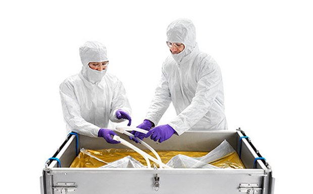 Two technicians in a sterile environment are operating a Mobius 2D and 3D single-use assembly system. They are dressed in full protective cleanroom suits, complete with hoods and masks, ensuring a contamination-free process.