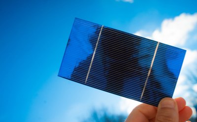 Solar cell capturing solar energy 单手握住一块蓝色太阳能电池薄板放在阳光下。