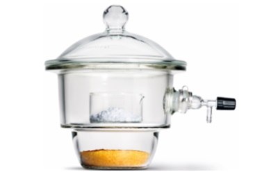  A round glass container with a tightly sealed lid that features a knob on top for easy handling. Inside the desiccator, there are two chambers: the upper chamber holds a small, transparent dish containing a white or grayish substance, likely a sample. The lower chamber contains an orange, granular material, a desiccant, which absorbs moisture. The desiccator is equipped with a side valve for vacuum connection, allowing for the removal of air to create a low-moisture environment. The entire apparatus is made of clear glass, giving it a sleek appearance.
