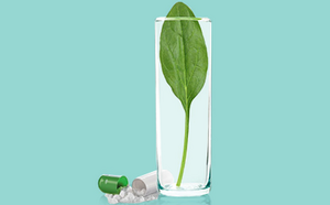 The image depicts a clear glass of water containing a single green leaf, surrounded by scattered pills and capsules. One of the capsules is open, revealing its powder contents.