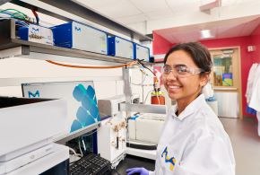Scientist in a lab setting wearing safety glasses standing in front of a large piece of equipment