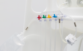 A medical manifold with five colored valves: red, yellow, green, blue, and purple. Each valve is connected to transparent tubing, extending from the manifold.