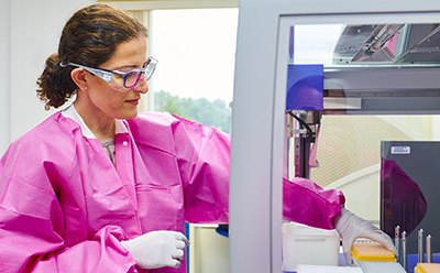 Female lab technician with lab protection cloth doing some testing activities with the help of a machine.