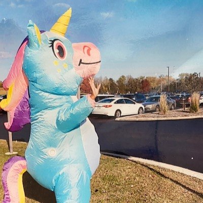 A blow-up unicorn — with Chevon Adams underneath — waves to the camera in the parking lot outside the Milwaukee site.