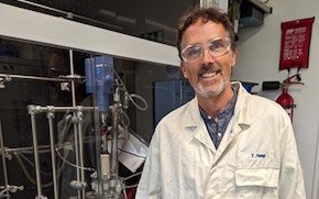 Haag lab tile Haag stands in the lab in a lab coat and wearing safety glasses.