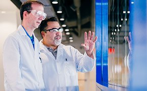 One scientist explaining new innovation to another scientist in front of a blue window