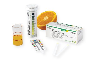 A citrus fruit and a beaker containing a liquid sample from the fruit which is subject to Ascorbic acid testing using MQuant® Ascorbic Acid Test Strips, alongside MQuant® Color Reference Card and packages of the test strips A citrus fruit and a beaker containing a liquid sample from the fruit which is subject to Ascorbic acid testing using MQuant® Ascorbic Acid Test Strips, alongside MQuant® Color Reference Card and packages of the test strips