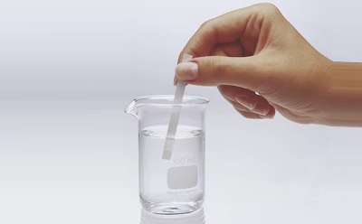 Chemist dips MQuant® test strip in a liquid contained in a small beaker to test a chemical parameter Chemist dips MQuant® test strip in a liquid contained in a small beaker to test a chemical parameter