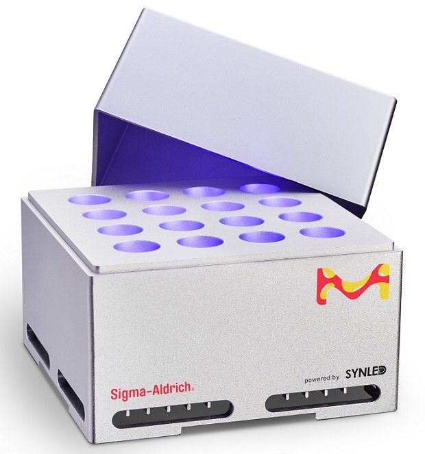 SynLED Parallel Photoreactor 2.0 against a white background. The device is a light grey cuboidal box with its cover partially open, revealing 16 vials illuminated by a 1 W blue LED centered at 467.5 nm, equipped with a 45° lens. The side facing the viewer displays a vibrant M logo in yellow and red at the top right corner.